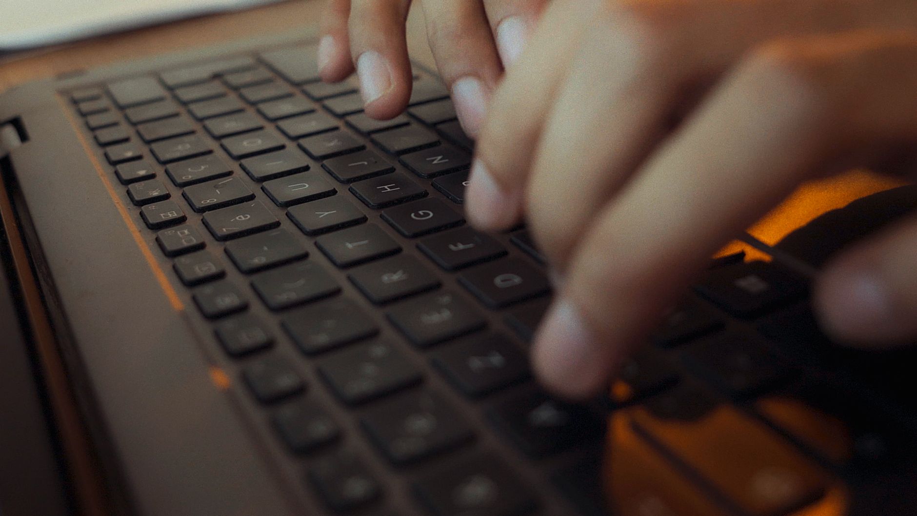 Hands typing on a laptop keyboard in low warm light