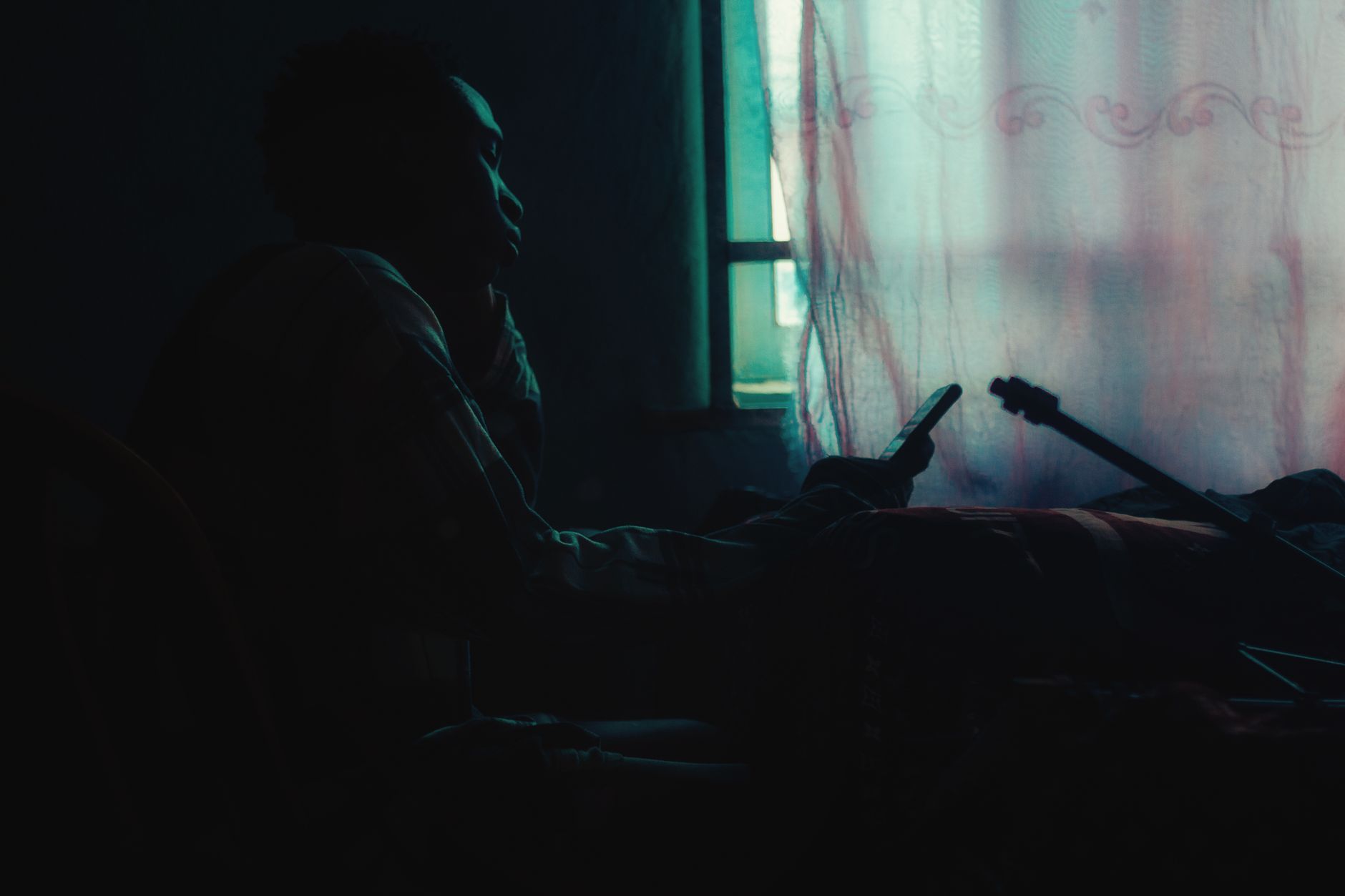 A person by a window at dusk, phone in hand, in silhouette