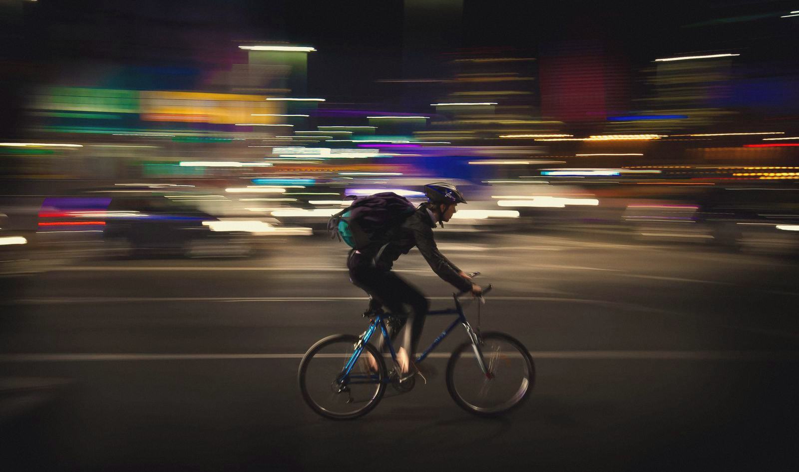 A night cyclist speeding past, the city lights streaked into colour behind