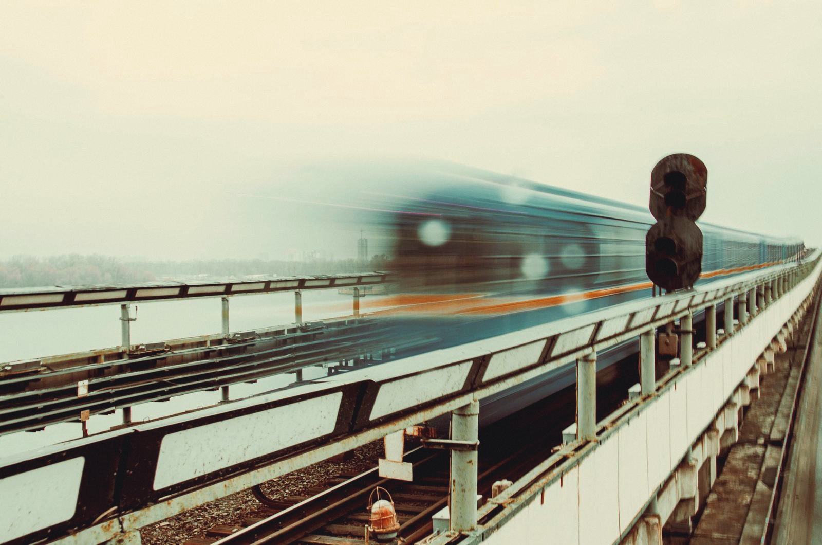 A teal train with an orange stripe blurred to pure motion, already gone
